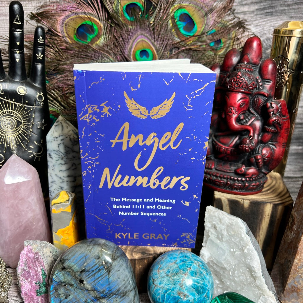 A book titled 'Angel Numbers' by Kyle Gray arranged with decorative items including crystals, a feather, and figurines.